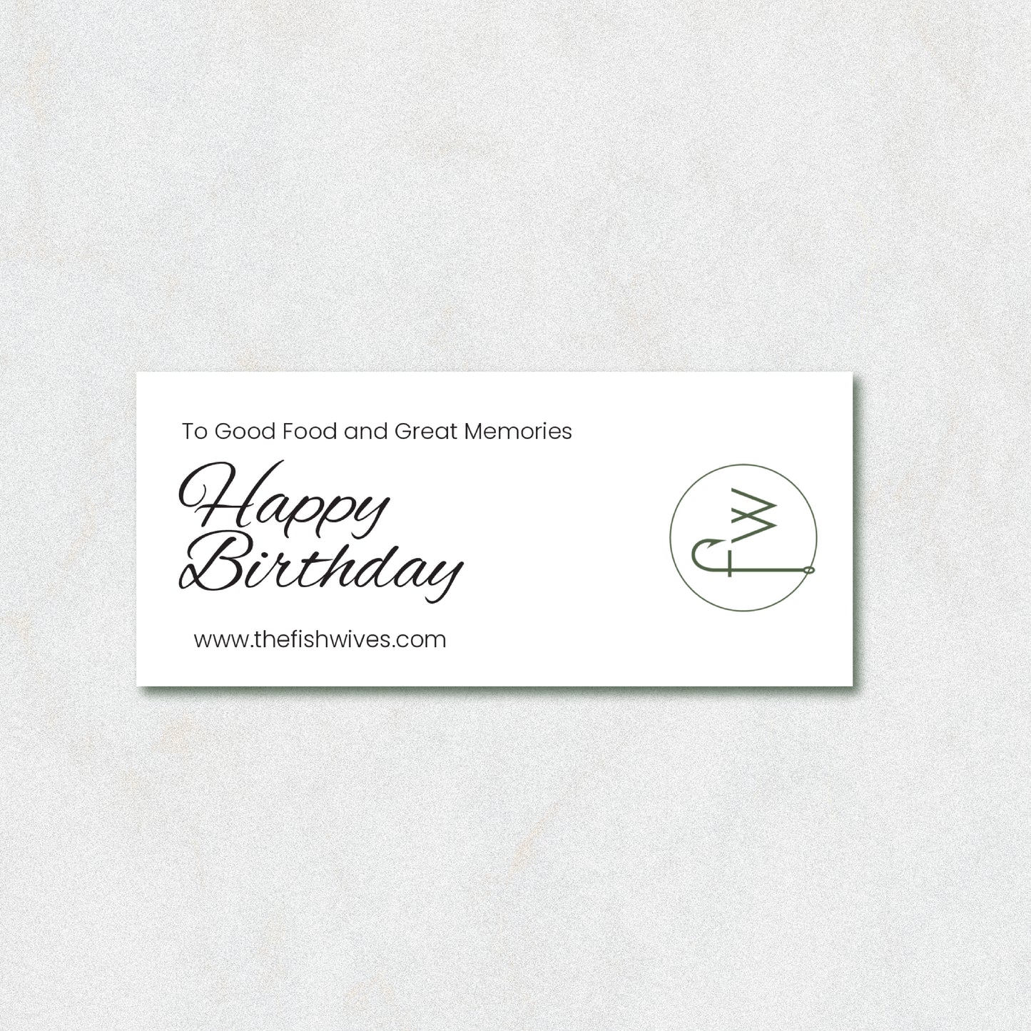 A rectangular white card with black text reading 'To Good Food and Great Memories Happy Birthday' and 'www.thefishwives.