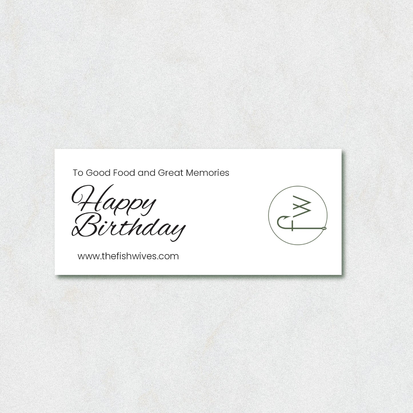 A rectangular white card with black text reading 'To Good Food and Great Memories Happy Birthday' and 'www.thefishwives.