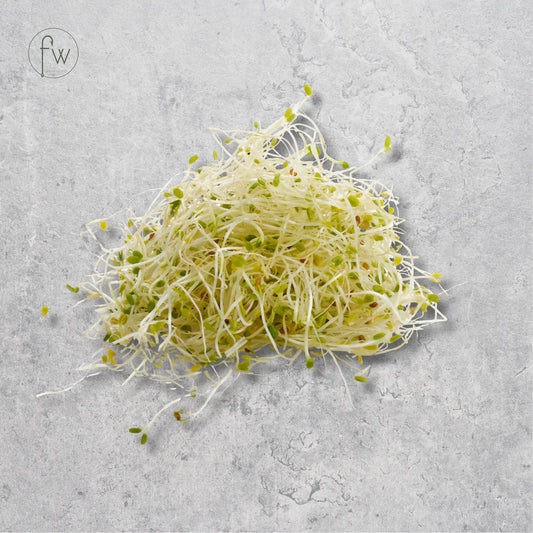 A small pile of fresh sprouts with pale white roots and light green tops, placed on a light gray textured surface. A small circular 'fw' logo appears in the upper left corner.