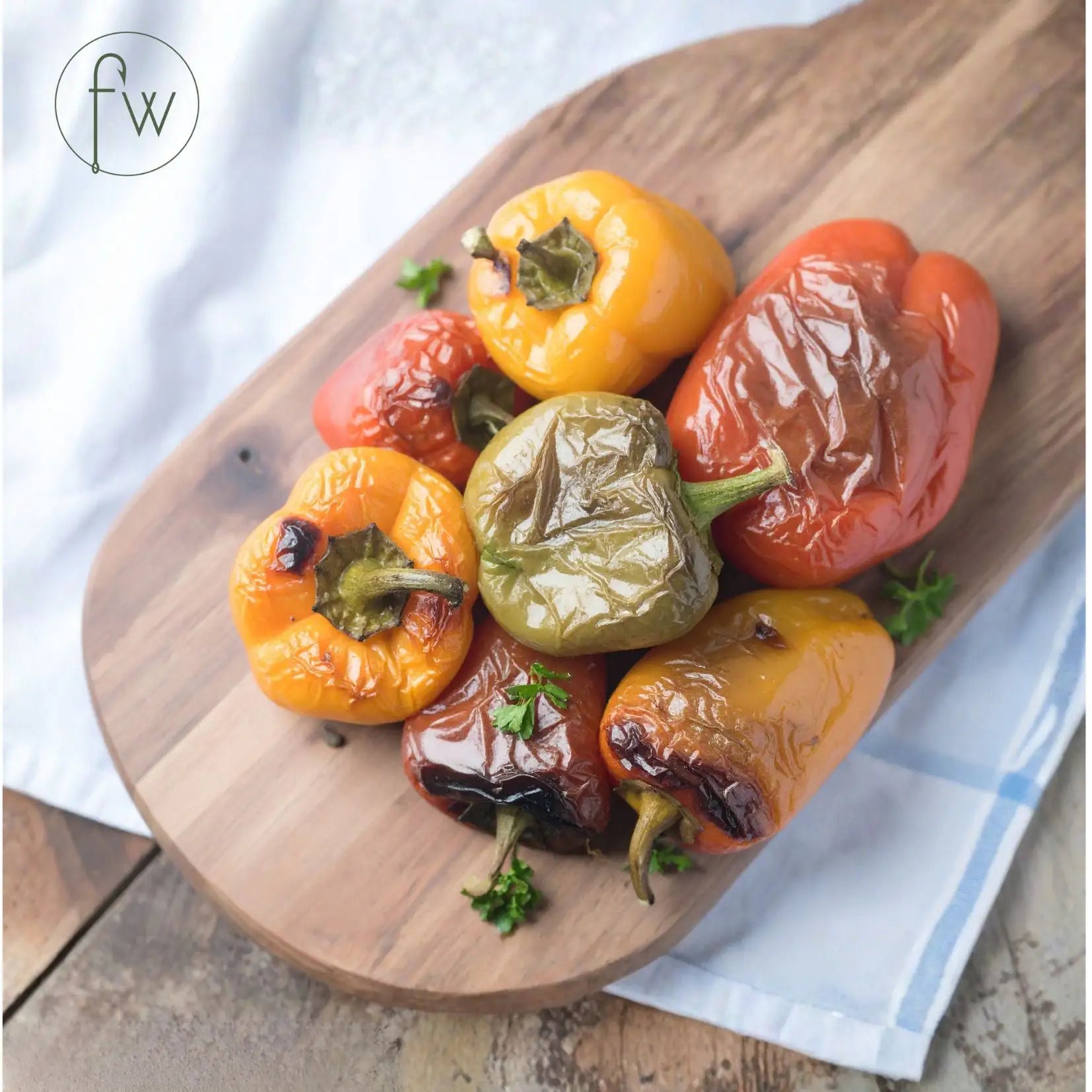 Roasted bell peppers on a wooden cutting board with a white cloth background