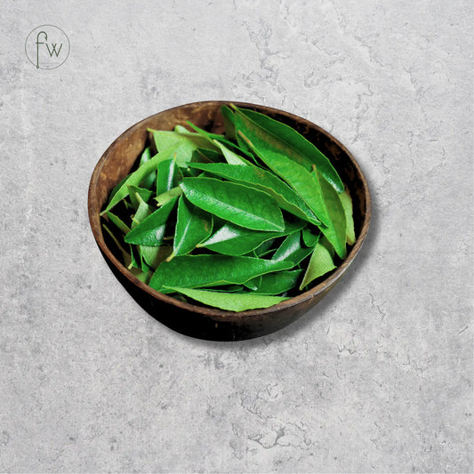 A dark brown wooden bowl filled with fresh green leaves, set against a textured gray concrete background with a circular 'fw' logo in the top-left corner.