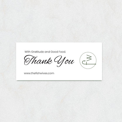 A rectangular white thank-you card with elegant black script reading 'Thank You' and smaller text 'With Gratitude and Good Food.' and 'www.