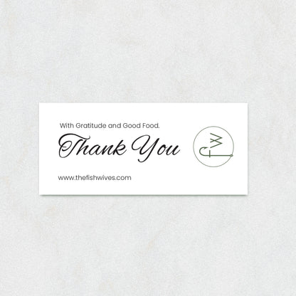 A rectangular white thank-you card with elegant black script reading 'Thank You' and smaller text 'With Gratitude and Good Food.' and 'www.