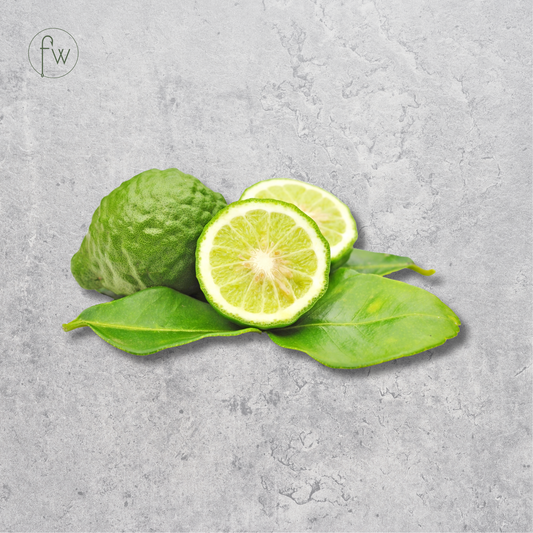 A green citrus fruit, shown whole and sliced open to reveal the juicy interior, resting on bright green leaves against a textured gray concrete background. A small circular 'fw' logo is visible in the top-left corner.