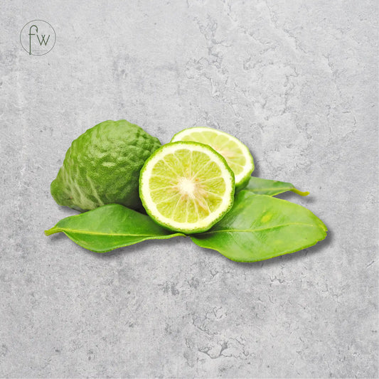 A green citrus fruit, shown whole and sliced open to reveal the juicy interior, resting on bright green leaves against a textured gray concrete background. A small circular 'fw' logo is visible in the top-left corner.