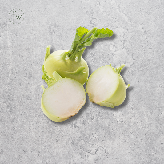 Three kohlrabi bulbs, with two cut open to show the pale white interior and green tops, arranged on a textured light gray surface. A small circular 'fw' logo appears in the upper left corner.
