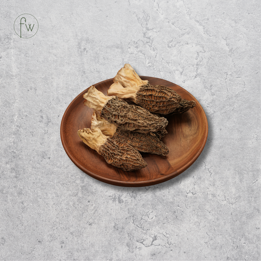 Four more mushrooms with beige stems and brown spongy caps, arranged on a round wooden plate against a textured light gray background.
