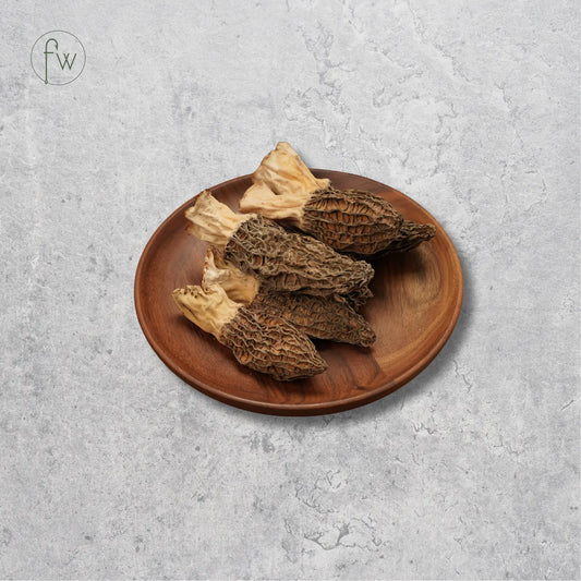 Four more mushrooms with beige stems and brown spongy caps, arranged on a round wooden plate against a textured light gray background.