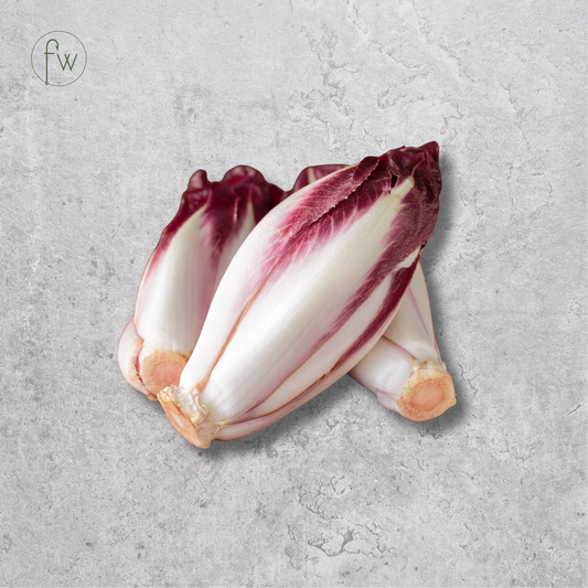 Three heads of red chicory lettuce with deep burgundy-red outer leaves and pale cream-white inner layers, arranged on a textured light gray surface. A small circular 'fw' logo appears in the upper left corner.