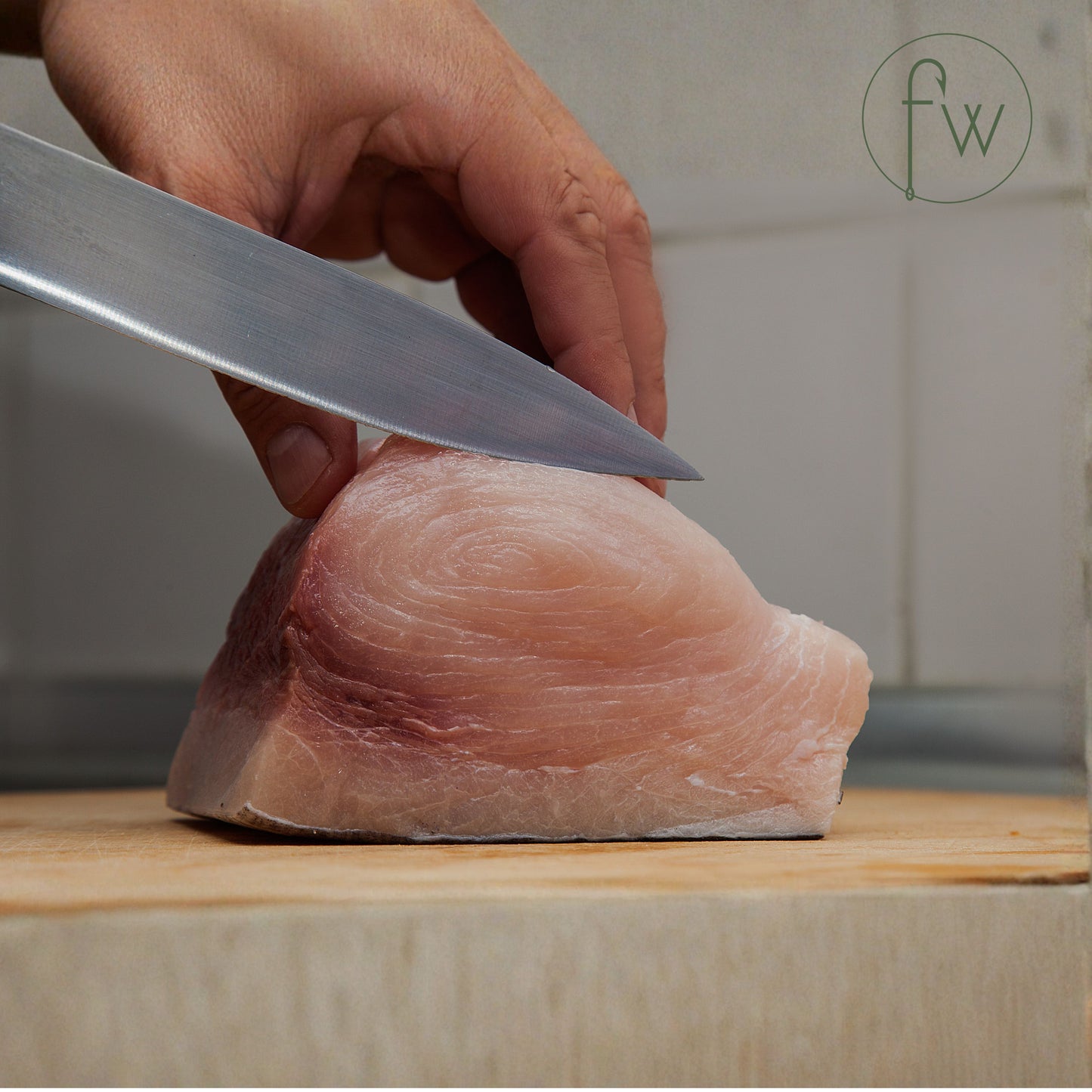 Person cutting Swordfish fish fillet with a knife on a wooden board