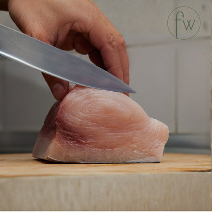 Person cutting Swordfish fish fillet with a knife on a wooden board