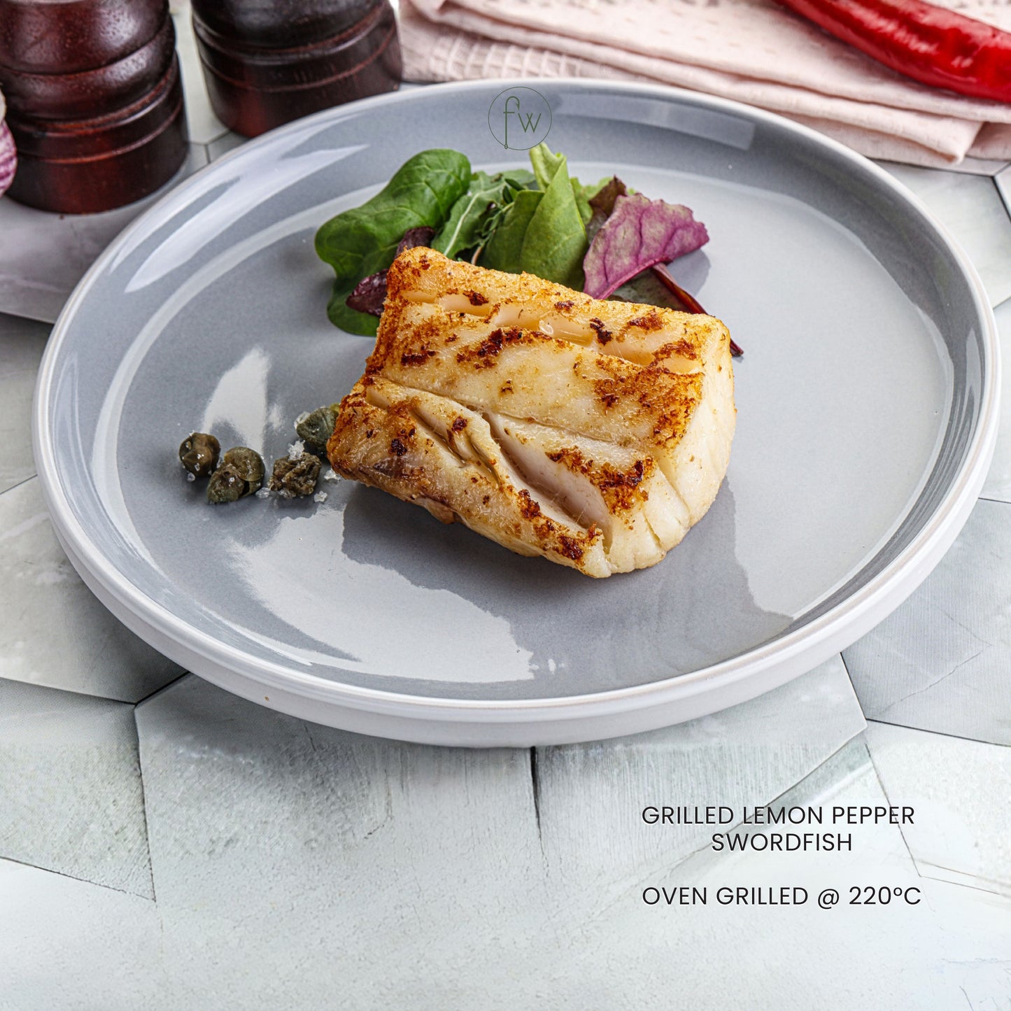 Grilled lemon pepper swordfish on a gray plate with salad, served on a light stone surface.