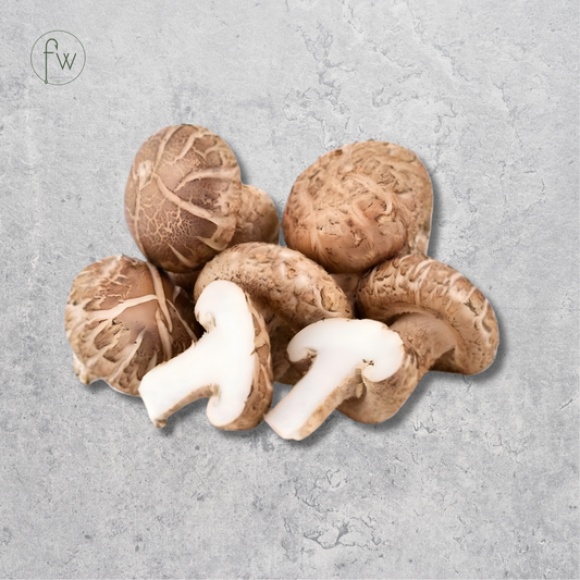 A cluster of fresh shiitake mushrooms, including two sliced pieces showing the white caps and tan gills, arranged on a textured light gray background. A small circular 'fw' logo is visible in the top-left corner.