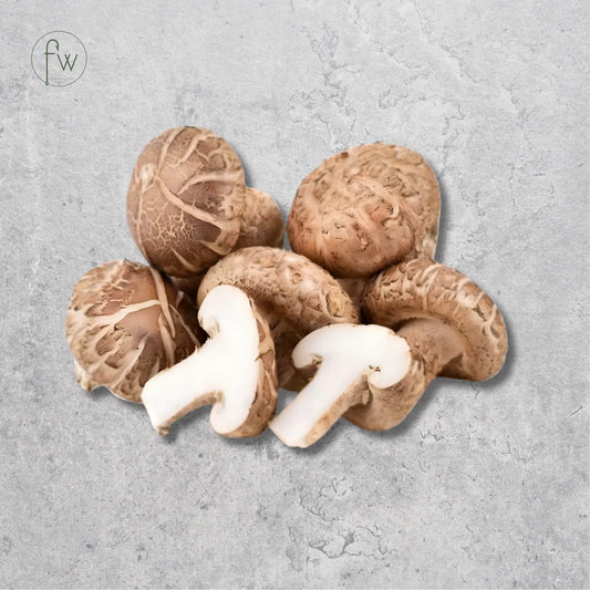 A cluster of fresh shiitake mushrooms, including two sliced pieces showing the white caps and tan gills, arranged on a textured light gray background. A small circular 'fw' logo is visible in the top-left corner.